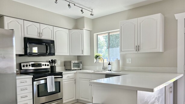 A modern kitchen with white cabinetry, stainless steel appliances, a large island, and a window providing natural light. - Downtown Gilbert *Pet-Friendly* Getaway (Gilbert)