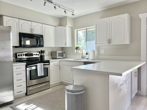 A modern kitchen with white cabinetry, stainless steel appliances, a large island, and a window providing natural light.
