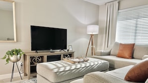 A living room with a flat-screen TV, a lamp, a sofa, an ottoman, and a potted plant. - Downtown Gilbert *Pet-Friendly* Getaway (Gilbert)