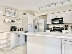 A modern kitchen with white cabinetry, a large island, stainless steel appliances, and a microwave.