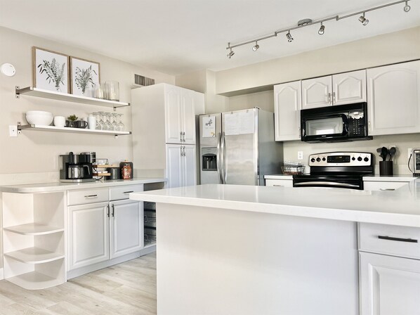 A modern kitchen with white cabinetry, a large island, stainless steel appliances, and a microwave.