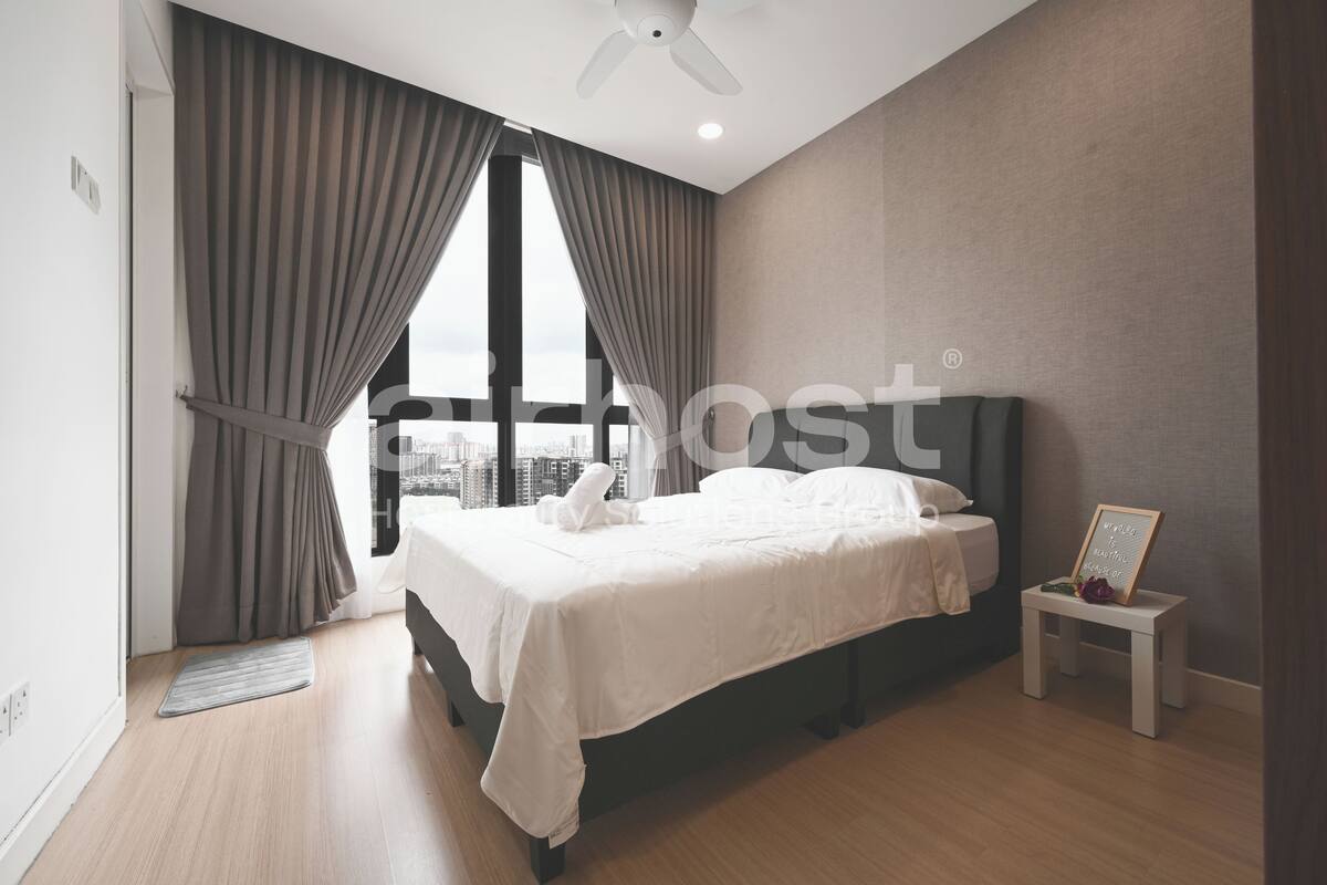 Ein modernes Schlafzimmer mit einem großen Bett, einem kleinen Nachttisch und Blick auf die Stadt durch große Fenster.