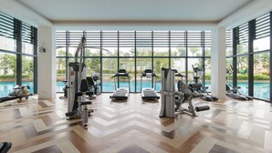 A modern gym with various exercise equipment, large windows, and a view of a swimming pool. - Greenfield Residence at Bandar Sunway (Petaling Jaya)