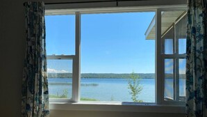 Habitación con un ventanal grande con vista a un lago, cortinas y un termostato a la vista.