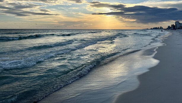 A beach with waves, a city skyline in the background, and a sunset. - Salty Air, Ocean Views, Private Heated Pool - Steps to the Sand (Panama City Beach)