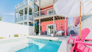 A two-story building with a swimming pool, outdoor seating, and a covered patio area. - Salty Air, Ocean Views, Private Heated Pool - Steps to the Sand (Panama City Beach)