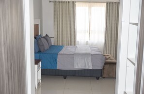 Ein Schlafzimmer mit Bett, Vorhängen, einer Bank und einem Nachttisch.