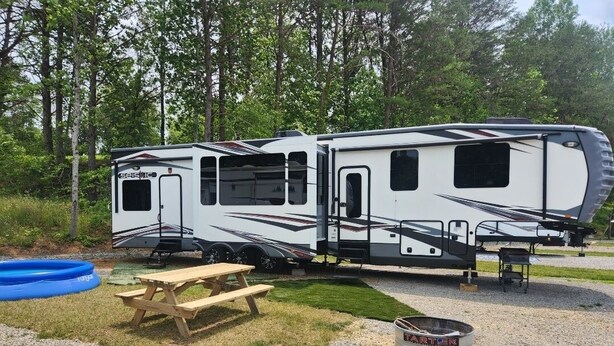 A recreational vehicle with a sliding door, a picnic table, a fire pit, and an inflatable pool. - Camper on campsite (Jamestown)