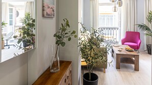 A modern living room with a wooden coffee table, a pink armchair, and a dining area with a table and chairs. There is a large mirror on the wall and a potted plant on the coffee table. - Malaga Center Flat - SoHo Center Apartments Superior (Málaga)