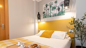 A neatly made bed with a yellow pillow, a checkered bedspread, and a tray with a cup and a pastry. - Malaga Center Flat - SoHo Center Apartments Superior (Málaga)