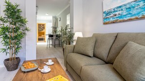 A modern living room with a sofa, a coffee table with pastries and cups, and a painting on the wall. - Malaga Center Flat - SoHo Center Apartments Superior (Málaga)