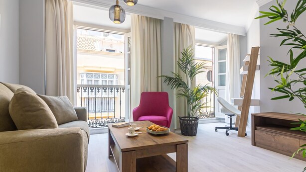 A modern living room with a sofa, a wooden coffee table, a pink chair, and a potted plant. - Malaga Center Flat - SoHo Center Apartments Superior (Málaga)