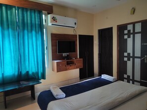 Ein Hotelzimmer mit Bett, Fernseher, Klimaanlage, Kleiderschrank und einer Bank.