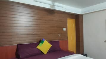 A hotel room with a wooden headboard, a purple bedspread, and a single yellow pillow.