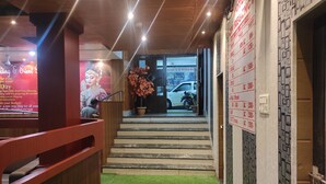 Un hall d’accueil d’hôtel avec un escalier menant à l’entrée, un comptoir de réception et un mur sur lequel est affichée une liste de prix.