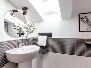 Ett modernt badrum med en vit tvättställ, en spegel, en krukväxt och en inramad tavla med ett giraffmotiv på väggen.
