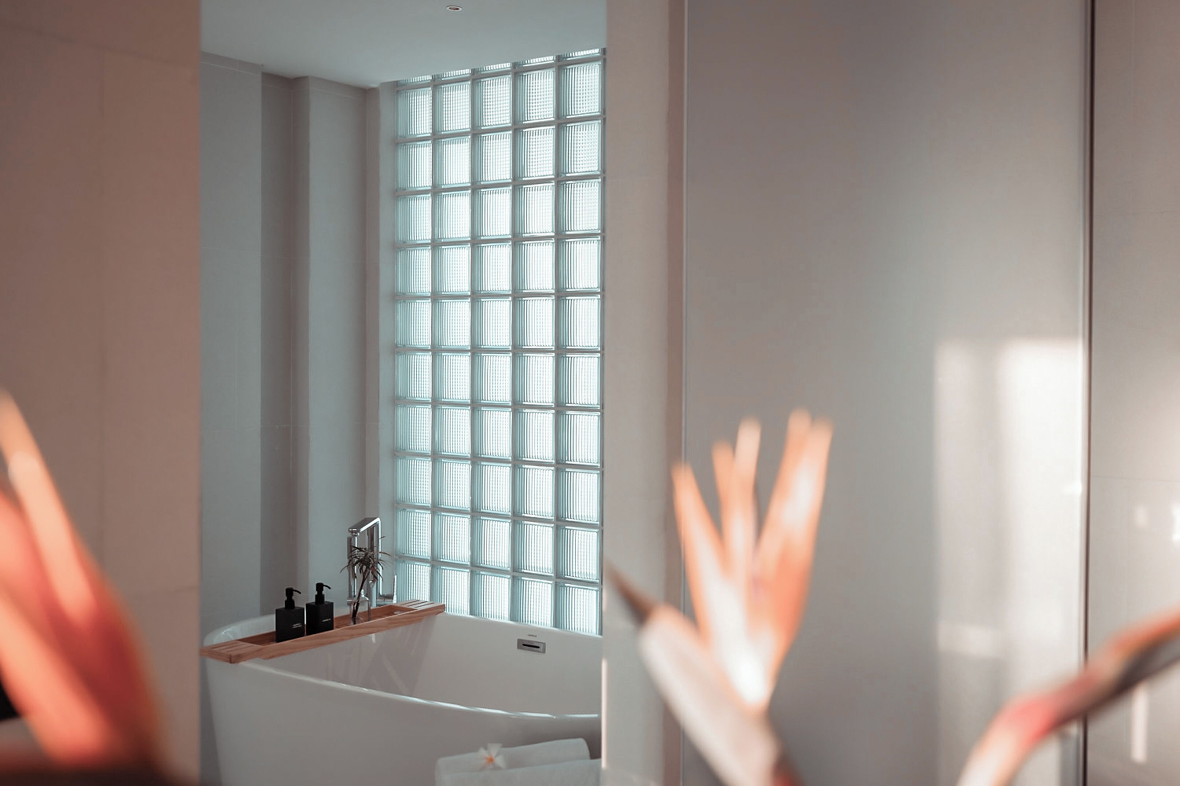 Un baño moderno con bañera, una ventana de diseño entramado y un estante de madera con artículos de aseo.