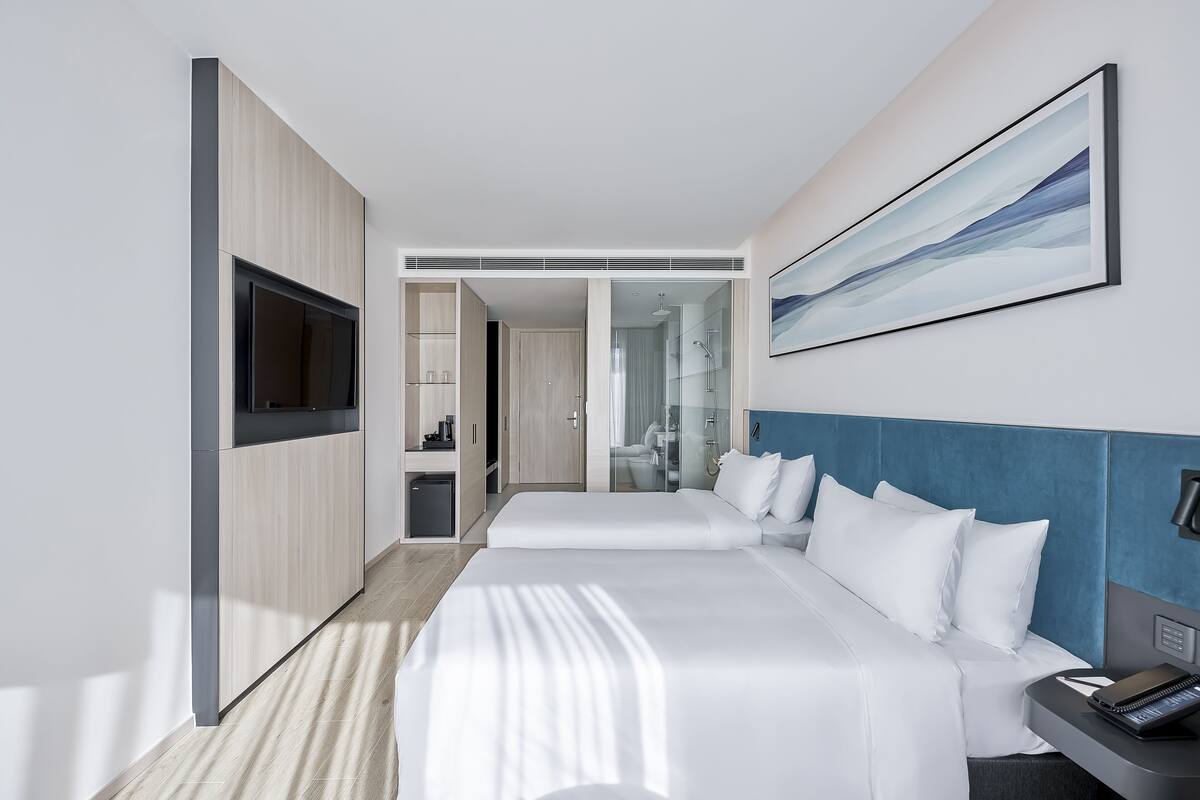 Habitación de hotel moderna con una cama grande, un televisor, un escritorio con teléfono, y un baño visible a través de una puerta abierta.