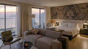 A modern hotel room with a large bed, a sofa, a dining table, and a view of the cityscape.