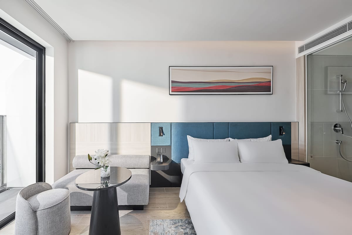 Una habitación de hotel moderna con una cama grande, un rincón de descanso con una mesita y un ventanal que ofrece vistas.