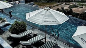 A rooftop pool area with lounge chairs and umbrellas, overlooking a cityscape and mountains.
