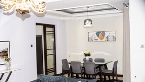 A modern living room with a gray sofa, a dining table with chairs, a chandelier, and a framed abstract painting on the wall.