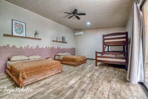 Une chambre avec deux lits, un ventilateur de plafond, un plancher en bois et un lit superposé.