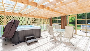 A wooden deck with a hot tub, outdoor seating, and large windows.