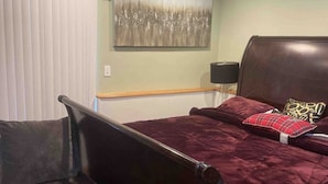 Un dormitorio con cama, un sillón oscuro, una mesita de noche con lámpara y un ventilador de techo.