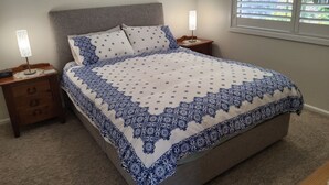 Een slaapkamer met een bed, nachtkastjes, een lamp, een schilderij en een raam met jaloezieën.