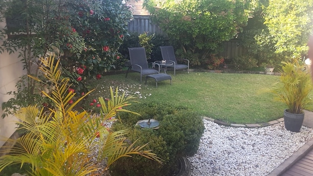 Een tuin met gazon, een klein vijverpartij en een zitgedeelte met stoelen.