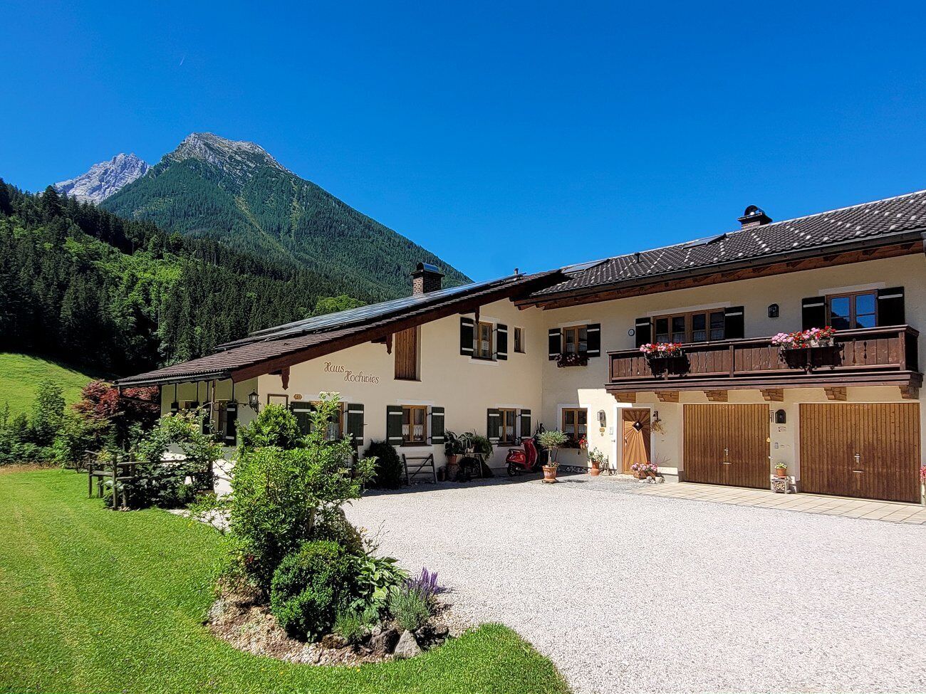 A two-story building with a balcony, a gravel driveway, and a mountain in the background.