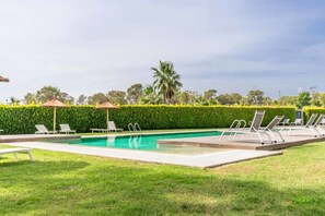 Ein rechteckiger Swimmingpool mit glasklar blauem Wasser, umgeben von einer niedrigen Hecke und einer Rasenfläche.