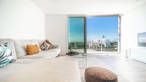 A modern bedroom with a large bed, a sofa, and a sliding glass door leading to a balcony with a city view. - Stunning Penthouse Apartment in Las Colinas - LS18LC (Las Colinas)