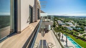 A modern building with large windows, a balcony with a glass railing, and a view of a residential area with houses and greenery. - Stunning Penthouse Apartment in Las Colinas - LS18LC (Las Colinas)