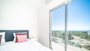 Une chambre avec un grand lit, une table de chevet et une vue sur le paysage urbain, visible à travers une porte vitrée.