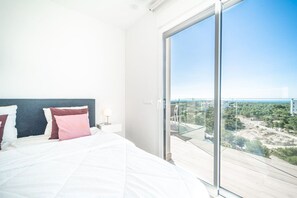 Een slaapkamer met een groot bed, een nachtkastje en een uitzicht op een stadsbeeld door een glazen deur.