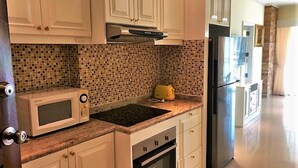 A kitchen with white cabinets, a microwave, a stove, and a refrigerator. - 1-bed in View Talay 5D - Sleeps 2 - Close to Beach (Pattaya)