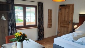 A bedroom with a bed, a table with a vase of flowers, a chair, a wooden door, and a window with curtains. - Appartement 1, Benedikt, 28qm (Prien am Chiemsee)