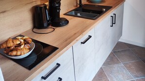 A modern kitchen with a wooden countertop, a coffee machine, a sink, and a bowl of pastries. - Appartement 1, Benedikt, 28qm (Prien am Chiemsee)