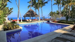 A pool area with lounge chairs, a thatched structure, and palm trees. - Villa Robalo Duplex - Villas del Palmar (Sayulita)