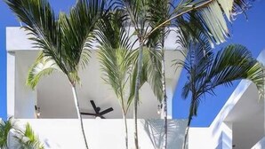 A modern building with a white facade, multiple balconies, and a central courtyard with palm trees and a ceiling fan. - Villa Robalo Duplex - Villas del Palmar (Sayulita)