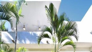Un bâtiment moderne à plusieurs niveaux, doté d’un vaste espace extérieur, de palmiers et d’un escalier menant à un niveau supérieur.