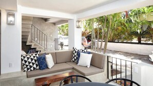 Un espace extérieur moderne aménagé avec un canapé et des fauteuils, un escalier et une vue sur les voitures garées et les palmiers.
