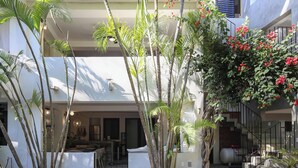 Un bâtiment moderne doté d’un toit plat, de nombreux balcons et d’une cour intérieure agrémentée de palmiers et d’un élément décoratif aquatique.