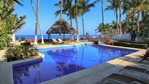 A swimming pool with lounge chairs, palm trees, and a view of the ocean. - Villa Robalo A - Villas del Palmar (Sayulita)