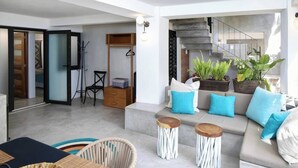 A modern living room with a sofa set, two side tables, a dining area with a table and chairs, and a staircase leading to an upper level. - Villa Robalo A - Villas del Palmar (Sayulita)