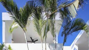 A modern building with a flat roof, large windows, and a central courtyard with palm trees and a ceiling fan. - Villa Robalo A - Villas del Palmar (Sayulita)