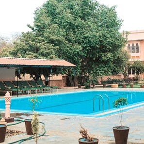 Relax by the serene pool surrounded by lush greenery and a traditional-style roof.