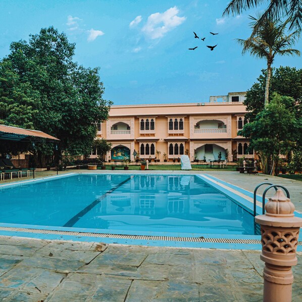 Relax by the serene pool surrounded by lush greenery and traditional architecture.
